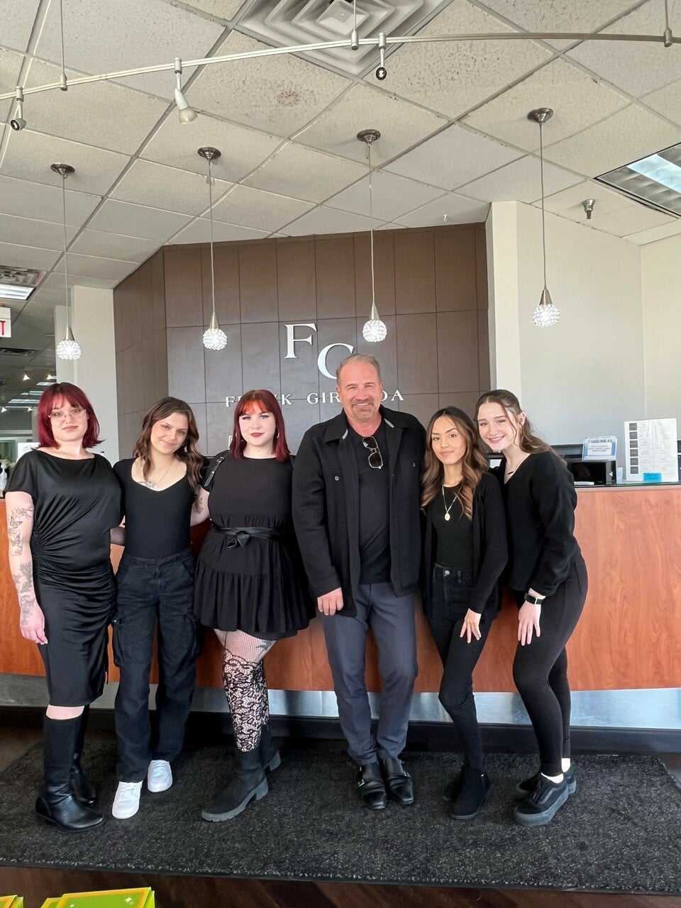 Group of six people standing in an office lobby, smiling for a photo.