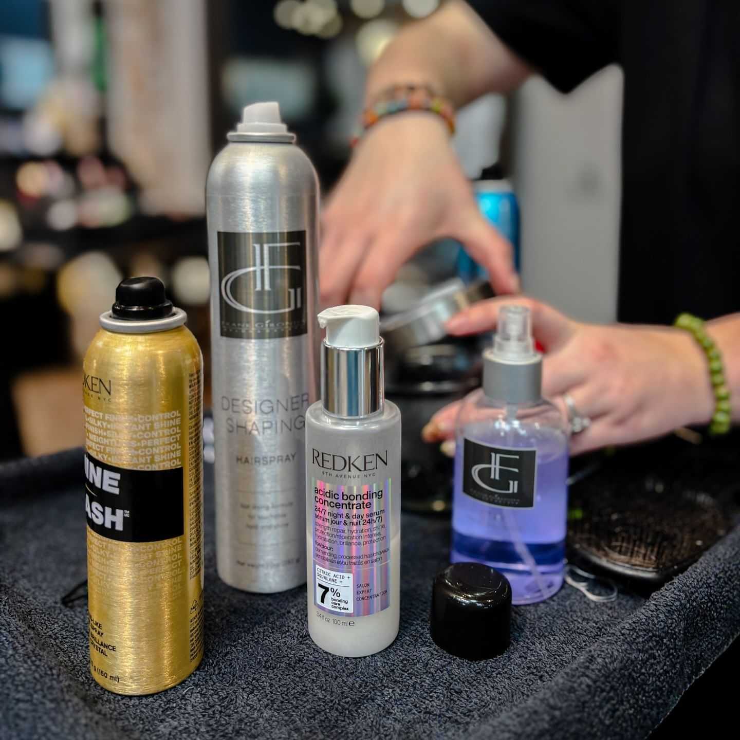 Haircare products on a salon counter with stylist's hands in the background.