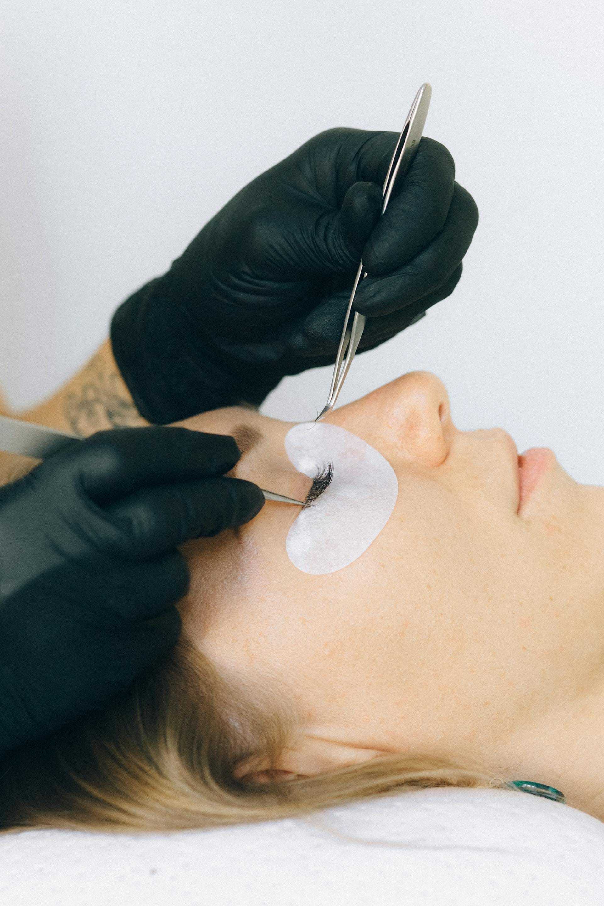 Gloved hands applying false eyelashes to woman's eye.