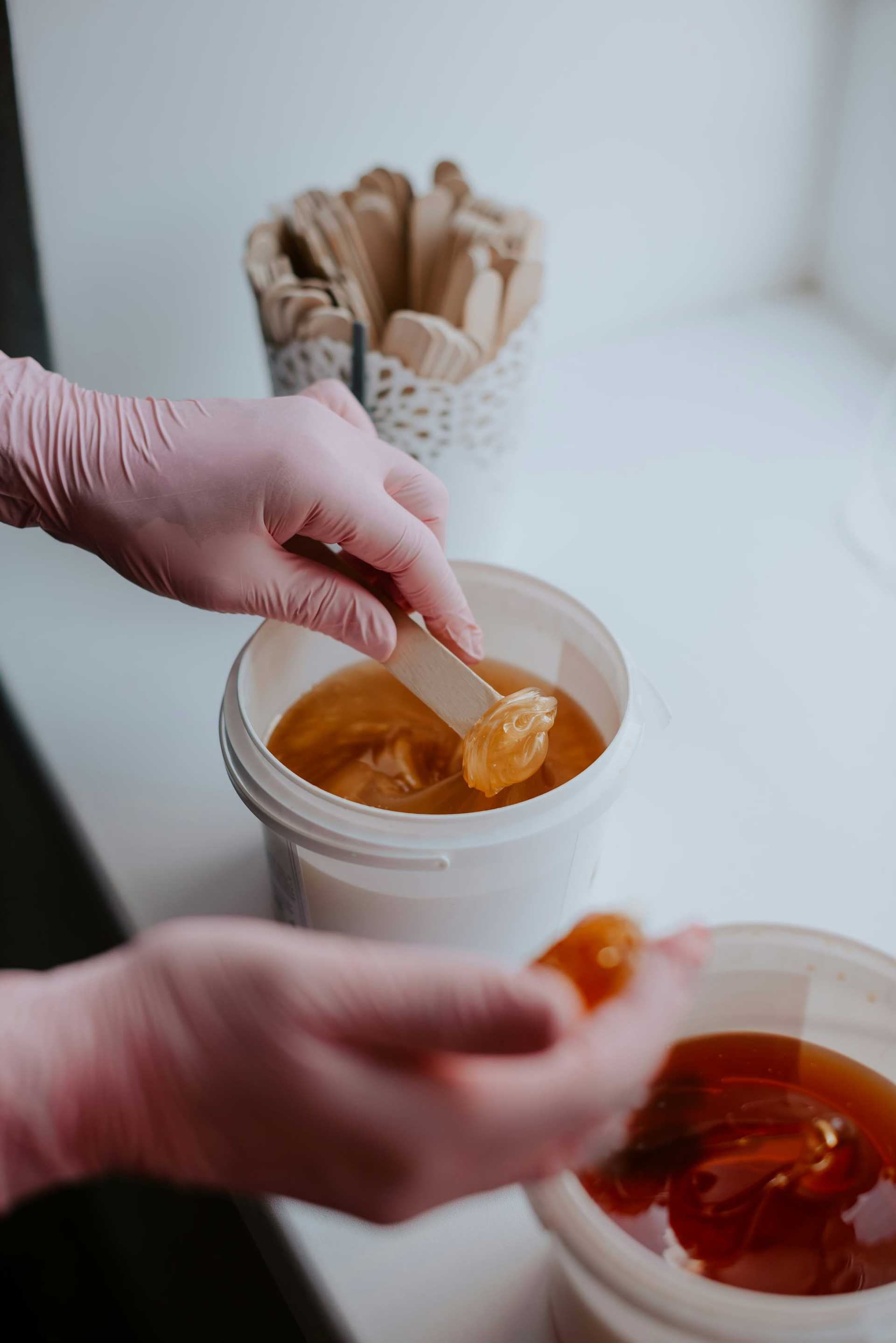 Person preparing waxing mixture with spatula and glove.